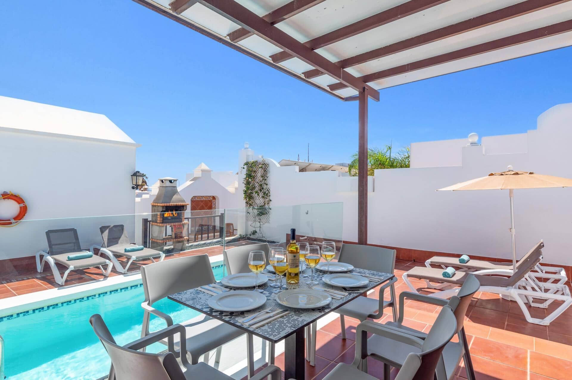 Un área de piscina en la azotea con una mesa lista para comer, sillas de descanso y una parrilla.