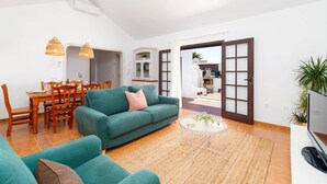 Una sala de estar moderna con un sofá color turquesa, una mesa de comedor con sillas y una mesita redonda con una planta.