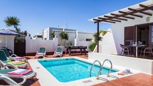 Zona de piscina en la azotea con sillones, una mesa y una pérgola.