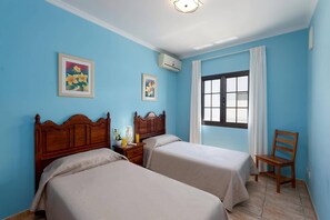 Habitación con dos camas, una ventana, una silla y dos unidades de aire acondicionado instaladas en la pared.