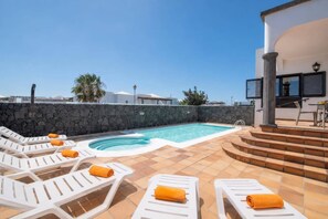 Un área de piscina con sillas de descanso y un muro de piedra.