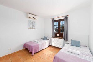 Un dormitorio con dos camas, una ventana con cortinas, un aire acondicionado instalado en la pared y un cuadro pequeño.