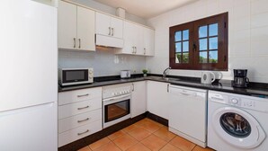 Uma cozinha compacta com armários brancos, micro-ondas, torradeira, cafeteira, forno e máquina de lavar.