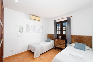 A room with two beds, a window with curtains, a wall-mounted air conditioner, and three framed artworks. - Villa Dorada by Villa Plus (Playa Blanca)