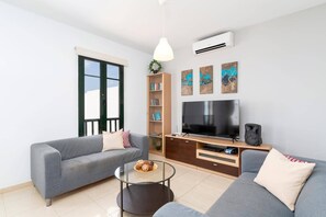 A modern living room with two grey sofas, a glass coffee table, a TV, a bookshelf, and an air conditioning unit.