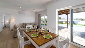 A dining area with a wooden table set for four, white chairs, and a view of a swimming pool through large glass doors.