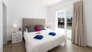 A modern bedroom with a large bed, two bedside tables, a nightstand, a window with curtains, and a view of the outdoors.
