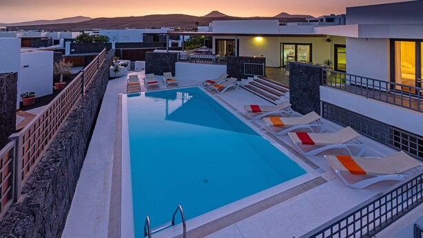 Une piscine sur le toit, dotée de chaises longues, d’un mur en pierre et offrant une vue sur le coucher de soleil et les montagnes.