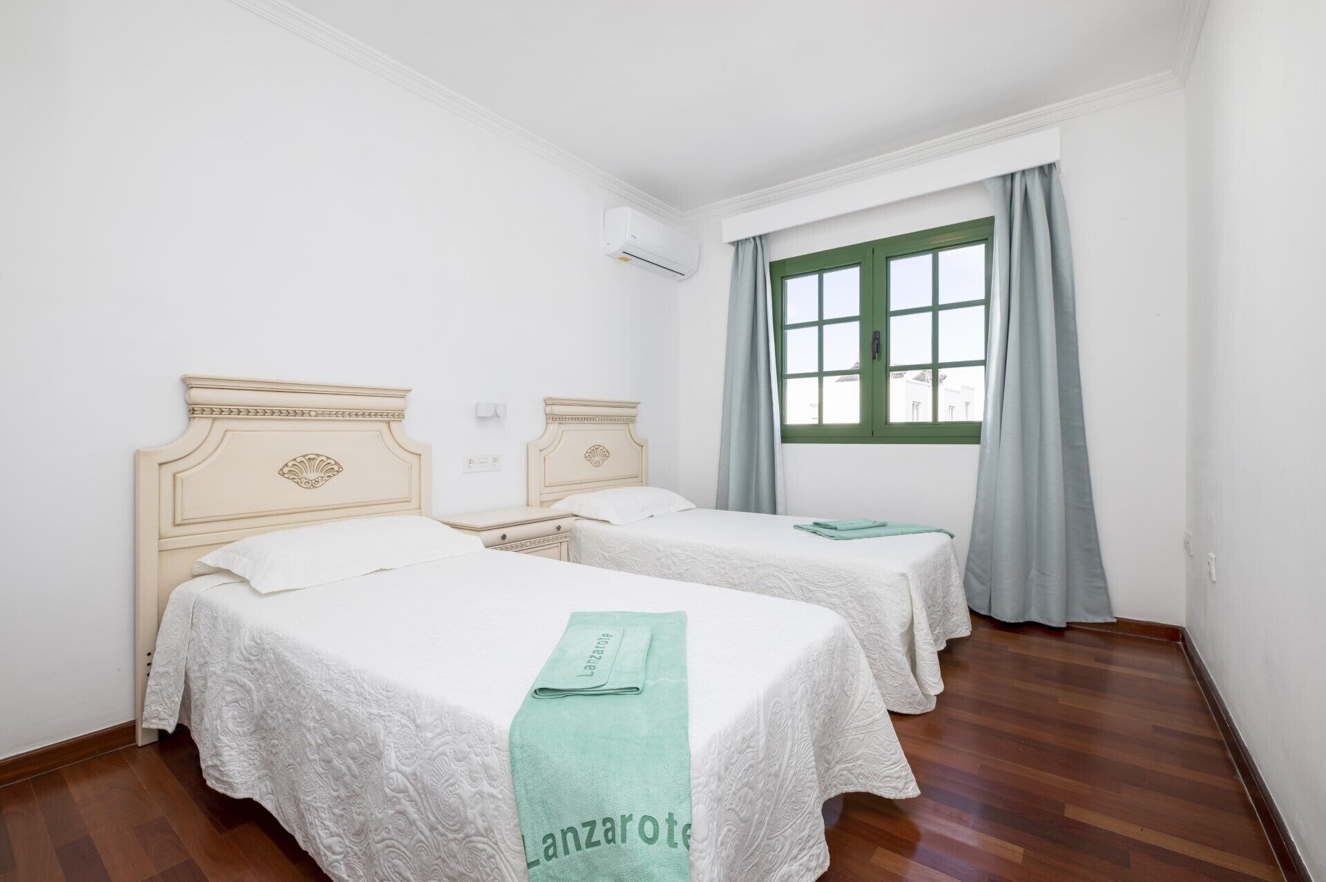 Habitació d'hotel amb dos llits, una finestra amb cortines verdes i un aparell d'aire condicionat a la paret.