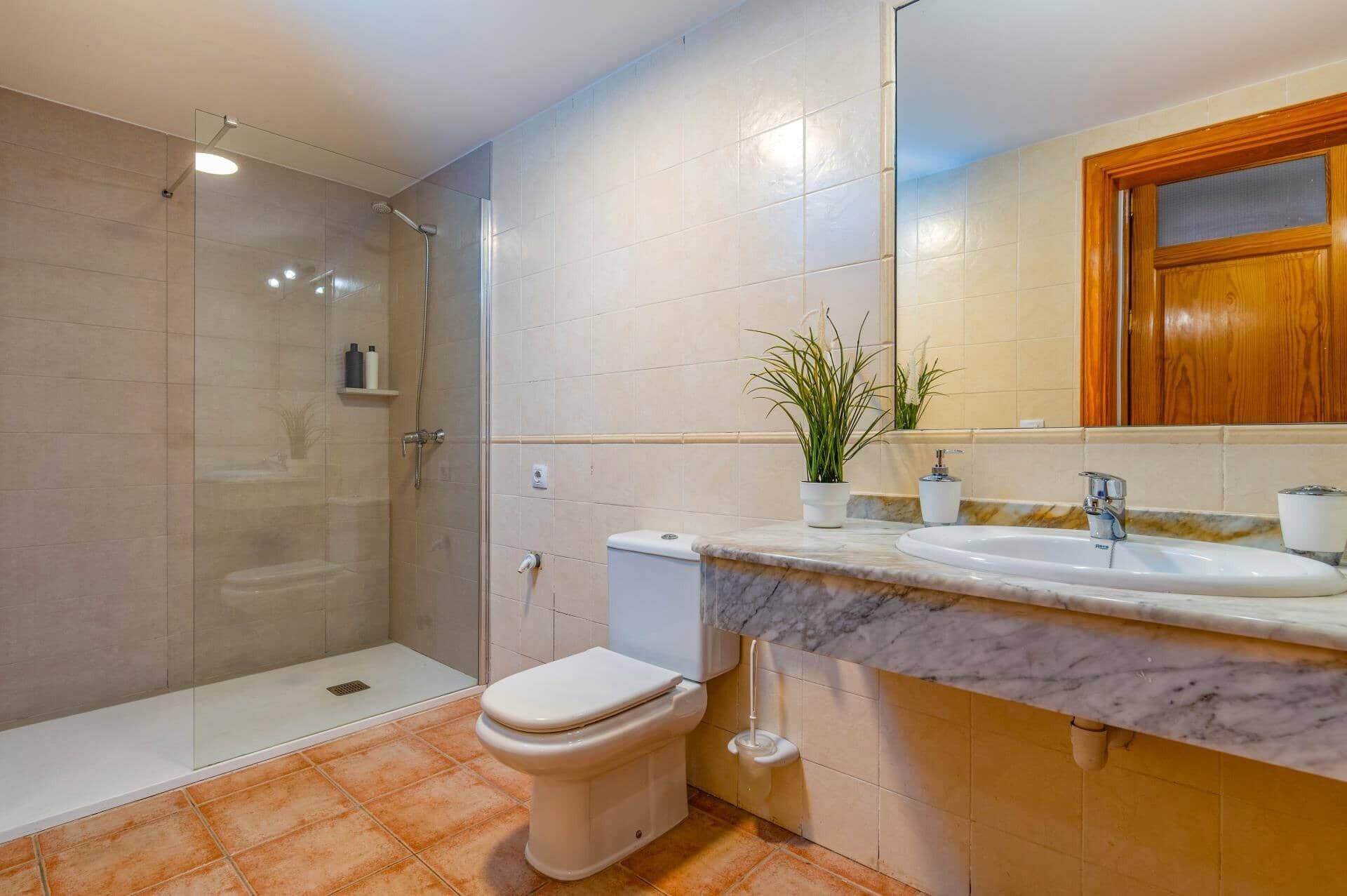 Ein Badezimmer mit Duschkabine, Toilette, Waschbecken mit Marmorplatte und Spiegel über dem Waschbecken.