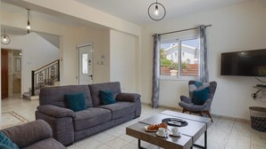 A living room with a grey sofa, a coffee table with a croissant, and a TV on the wall. - Villa Dione by Villa Plus (Peyia)