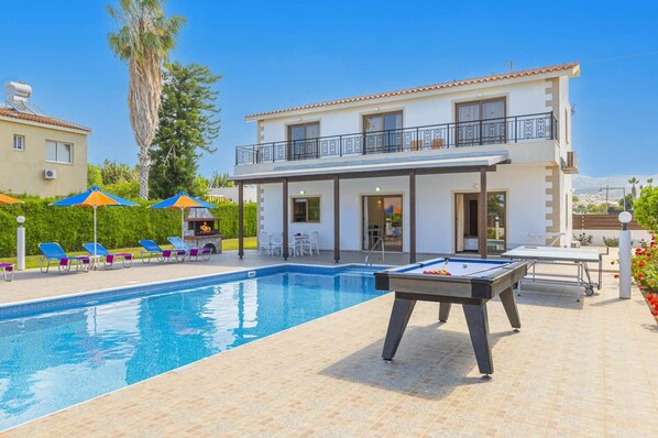 A pool area with a table tennis table, lounge chairs, and a barbecue. - Villa Heracles by Villa Plus (Peyia)