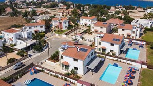 Ett bostadsområde med villor, en swimmingpool och utsikt över havet.