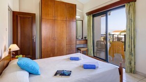Ett hotellrum med en säng, en garderob, ett skrivbord, en stol och en balkong med gardiner.