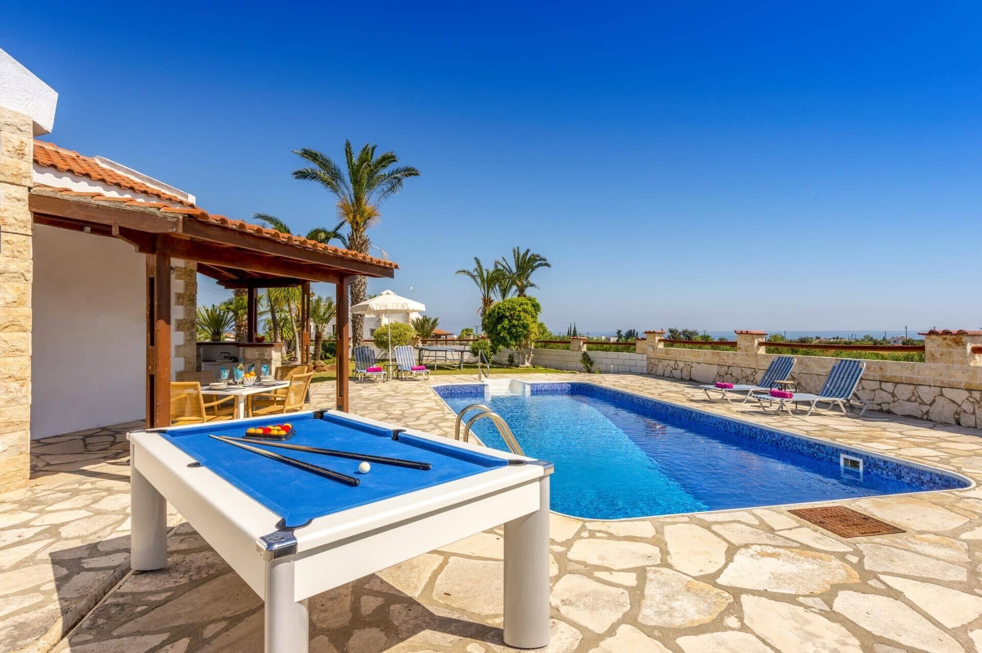 A pool area with a pool table, lounge chairs, and a pergola.