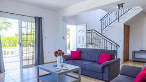 A spacious living room with a grey sofa, a coffee table, and a staircase leading to an upper floor. - Villa Giota by Villa Plus (Peyia)