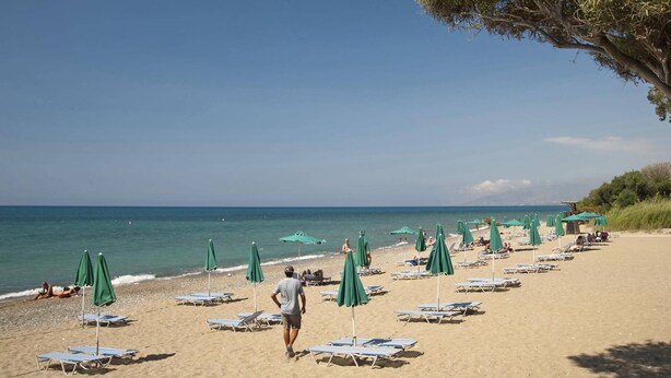 A beach with rows of sun loungers and green umbrellas, a clear sky, and the ocean in the background. - Villa Ibiscus by Villa Plus (Poli Crysochous)