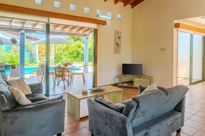 A living room with a sofa, coffee table, TV, and a patio area with a pool and outdoor seating.