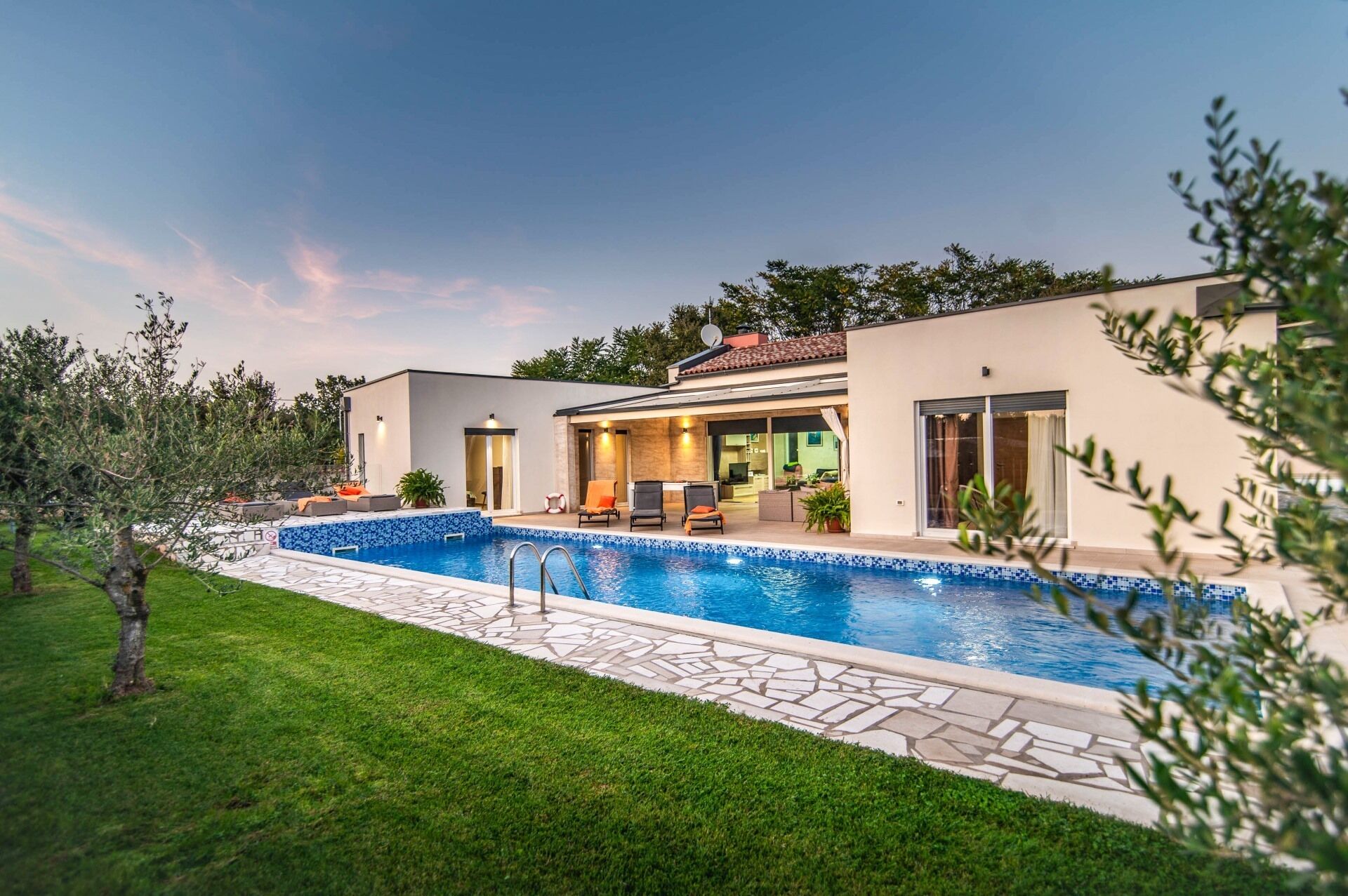 Une maison moderne dotée d’une piscine, d’un patio couvert et d’une pelouse bien entretenue.