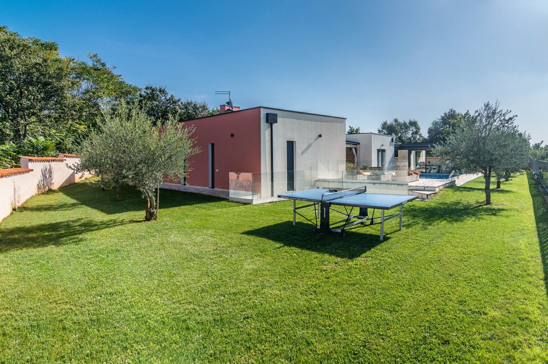 Ett modernt utomhusområde med ett bordtennisbord, en swimmingpool och en liten byggnad med en röd fasad.