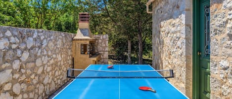 Ein Tischtennis-Tisch im Freien vor einer Steinwand und einem dahinterliegenden Steinhaus.