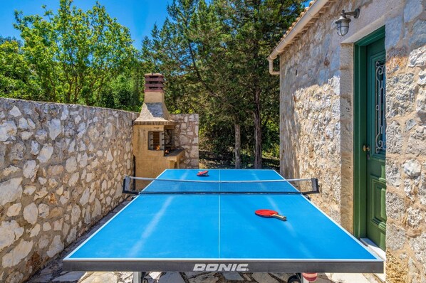 An outdoor ping pong table with a stone wall and a stone building in the background. - Villa Delfini by Villa Plus (Antipata)