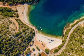 Vista aérea de una zona costera con playa, agua cristalina, barcos y un estacionamiento.