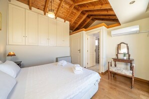 Un dormitorio con una cama grande, una mesita de noche, una lámpara, un aparador de madera, un espejo y una puerta que da a otra habitación.