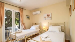 Ein Hotelzimmer mit zwei Betten, einer Schiebetür, einer Klimaanlage und einem kleinen Nachttisch mit einer Lampe.