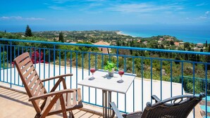 Ein Balkon mit Tisch, zwei Stühlen und Blick auf das Meer und die Landschaft.