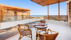 A balcony with wicker chairs and a table, overlooking a stone building and a clear sky. - Villa Angelina Olivestone by Villa Plus (Rhodes)