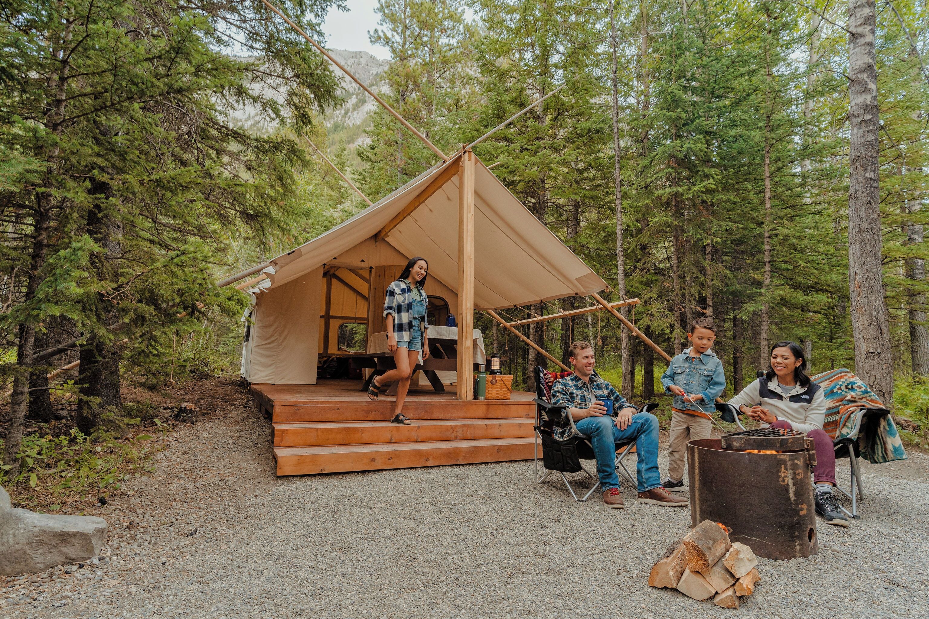 A tent with a wooden deck, a fire pit, and a forested backdrop.