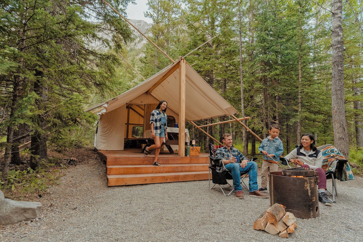A tent with a wooden deck, a fire pit, and a forested backdrop.
