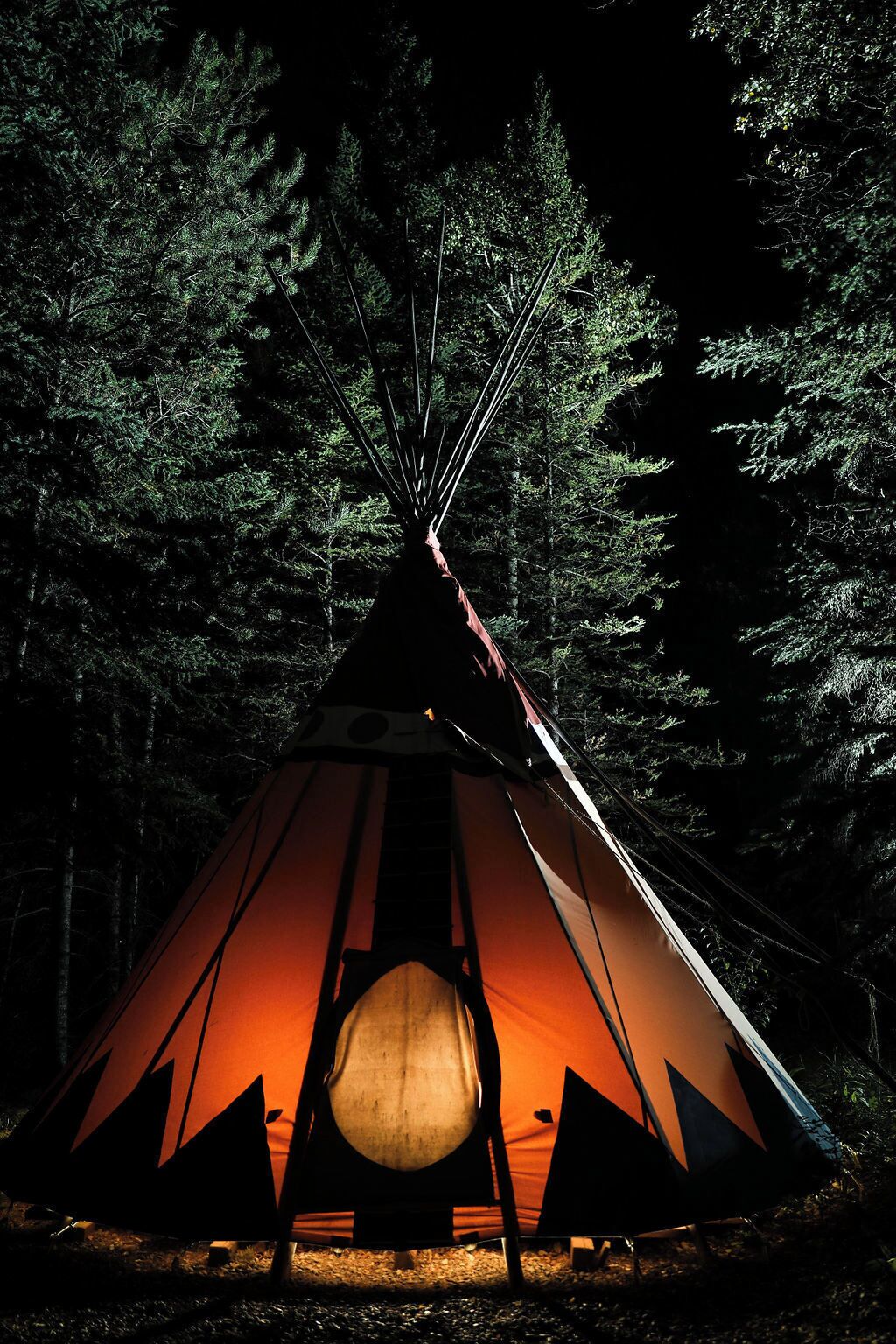 A teepee with a circular fire pit in the center, surrounded by dense forest.