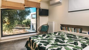 Une chambre avec un grand lit, une télévision, une bibliothèque et une vue sur un jardin.