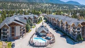 A resort with multiple buildings, a central pool area, and a mountainous backdrop. - Red Spruce | Hot Tub | Pool | King Bed (Radium Hot Springs)
