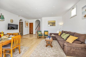 A living room with a sofa, a dining table, chairs, a TV, and a staircase.