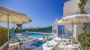 Un espace aménagé au bord de la piscine, avec des chaises longues, une table à manger pour deux personnes et un anneau de sauvetage fixé au mur.