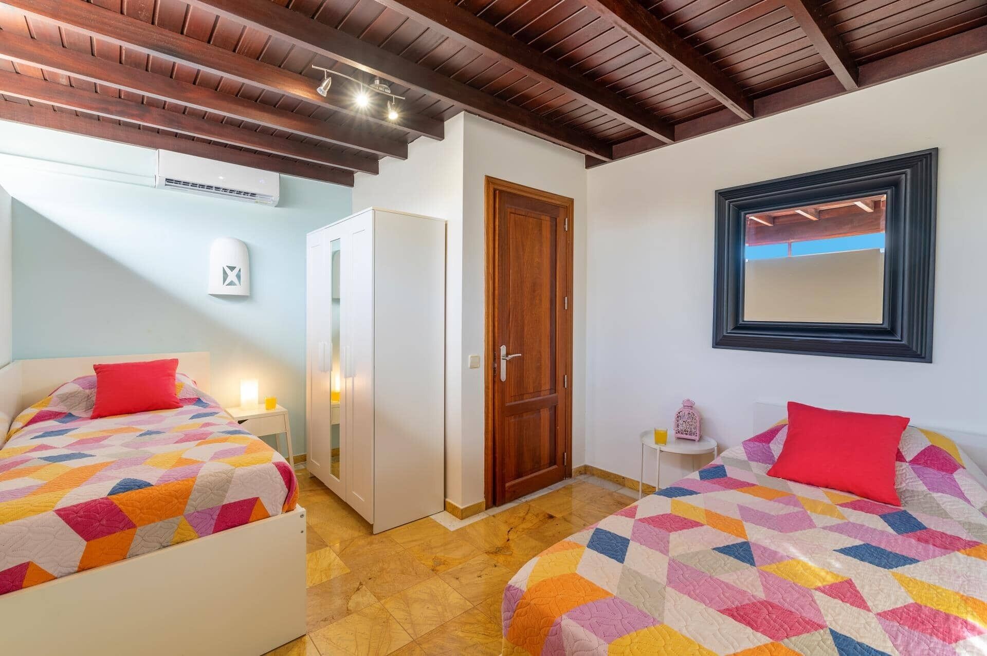 Ein Hotelzimmer mit zwei Betten, einer Holzbalkendecke, einem weißen Kleiderschrank, einer Holztür und einem gerahmten Spiegel an der Wand.