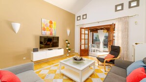 Sala de estar com televisão, sofá, mesa de centro e vista para o exterior.