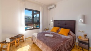 Quarto com cama, janela, uma mesinha e aparelho de ar condicionado.