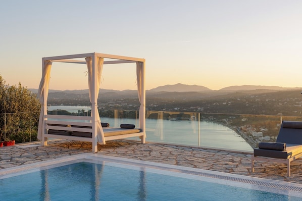 Area piscina con una pergola bianca, poltrone da relax e vista sulle montagne e un ponte.