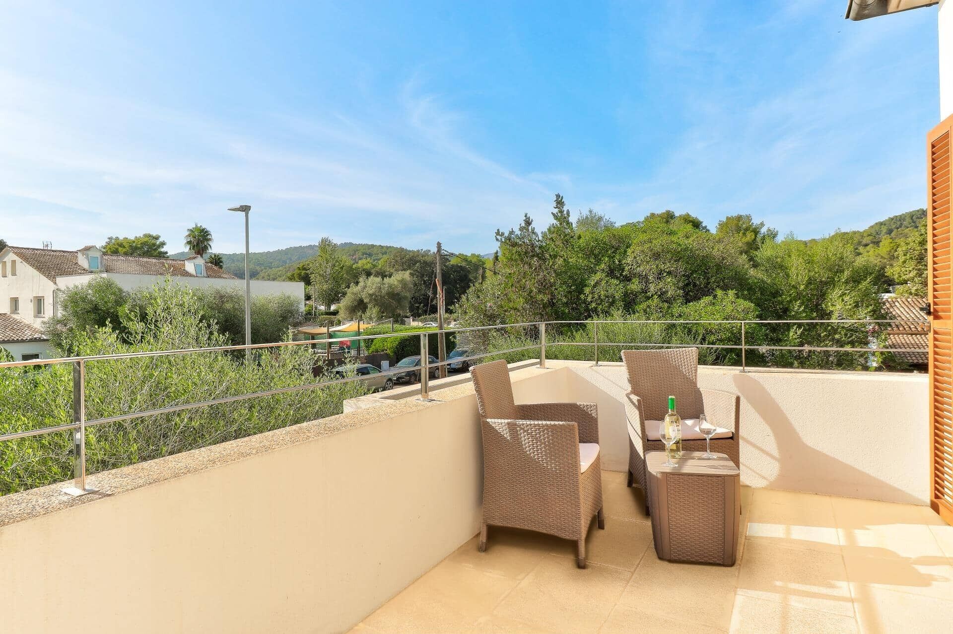 Un balcon doté de meubles en osier et d’une table, offrant une vue sur un quartier résidentiel avec ses maisons et sa verdure.