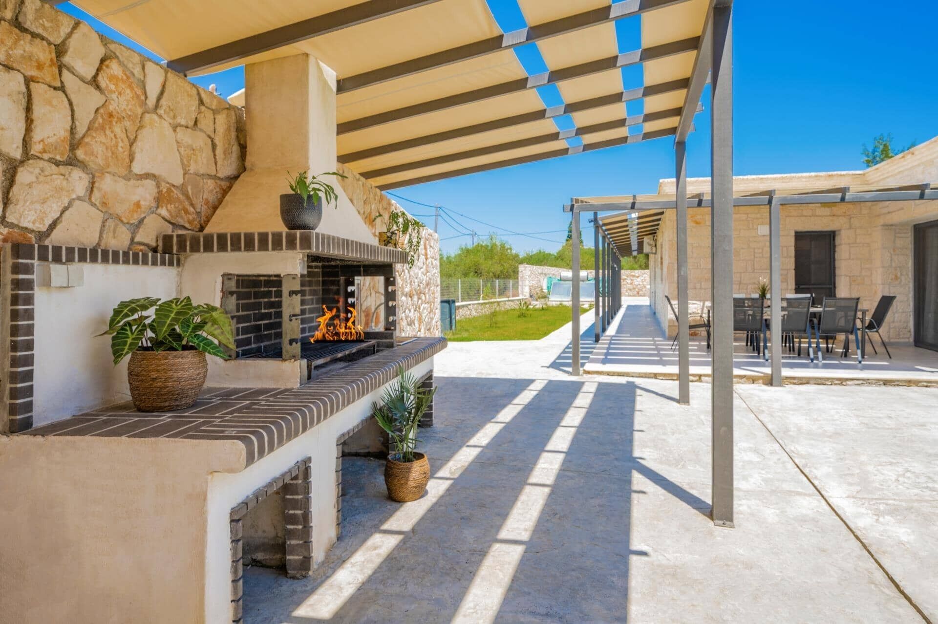 Une terrasse extérieure dotée d’une cheminée en pierre, d’un espace salon et d’une partie couverte avec des tables et des chaises.