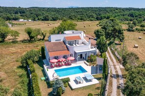 Une maison moderne à deux étages avec une piscine, située au cœur d’un paysage rural.