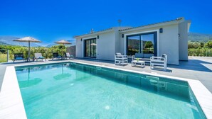 Una casa moderna con piscina, zona de estar exterior y vistas a la montaña.