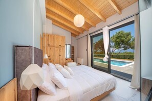 A bedroom with a large bed, wooden ceiling beams, a view of a swimming pool, and a sliding glass door. - Villa Drogarati Cottage by Villa Plus (Cephalonia)