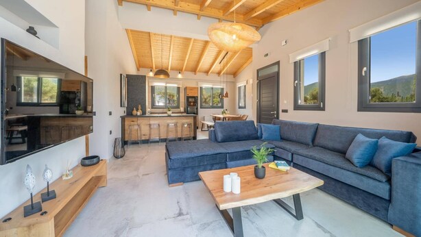 Una sala moderna con un sofá grande, una mesa de centro y una cocina visible a través de una puerta abierta.