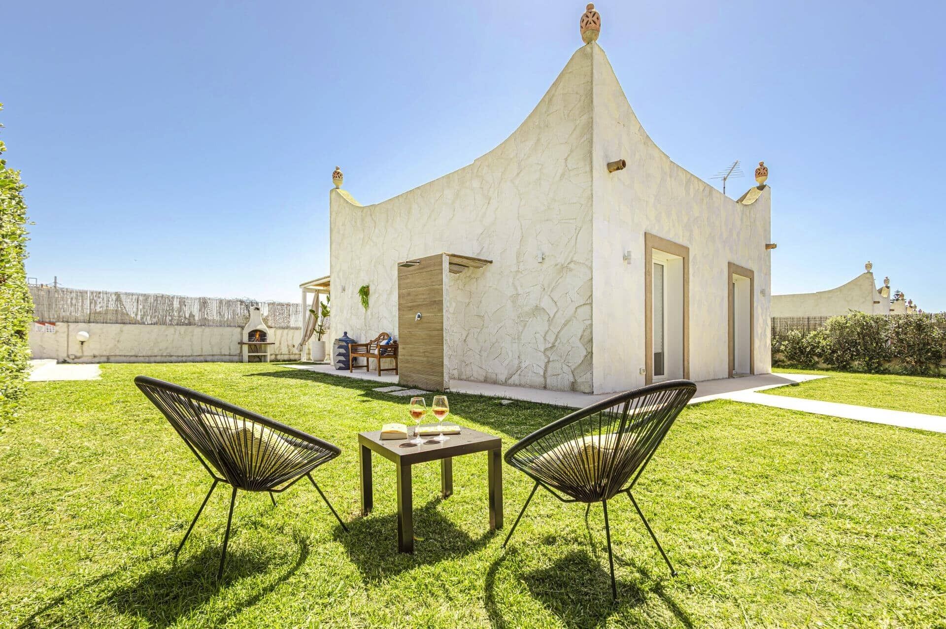 A modern building with a unique architectural design, a small patio area with two chairs and a table, and a clear sky.