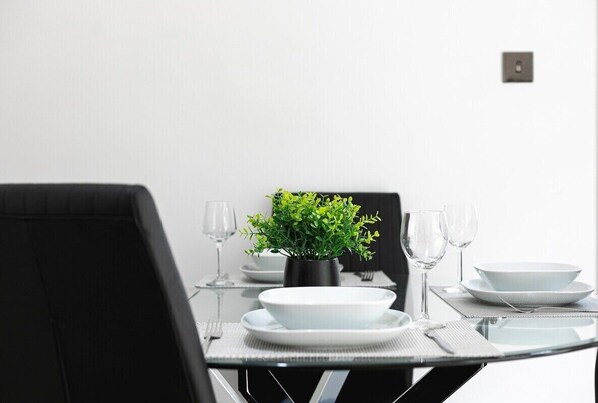 Ett matbord dukat med vita tallrikar, skålar och glas, en liten krukväxt och en svart stol.